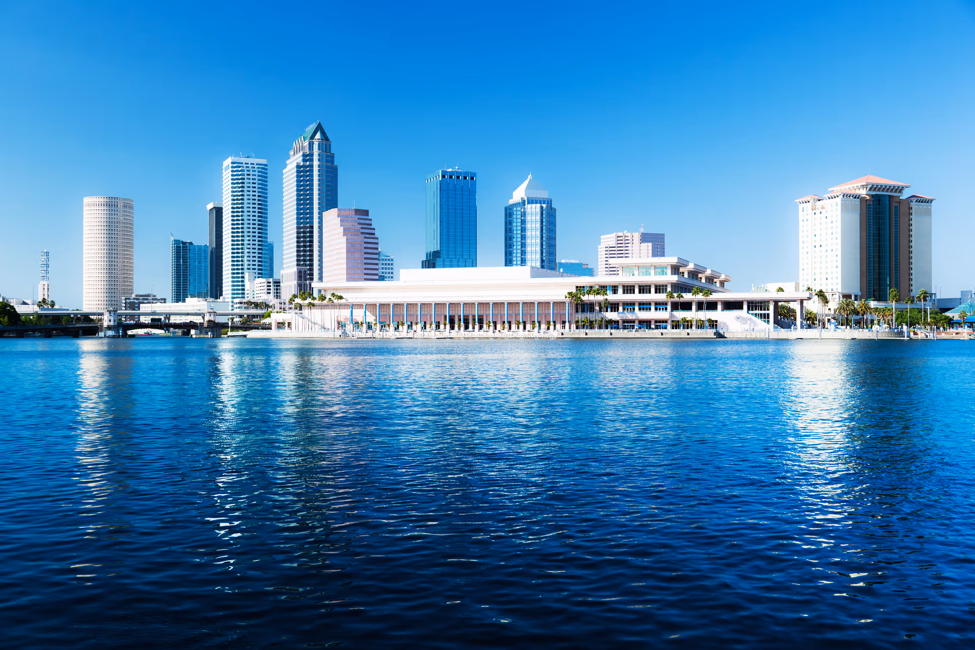 City skyline with tall buildings along a calm blue waterfront under clear sky.
