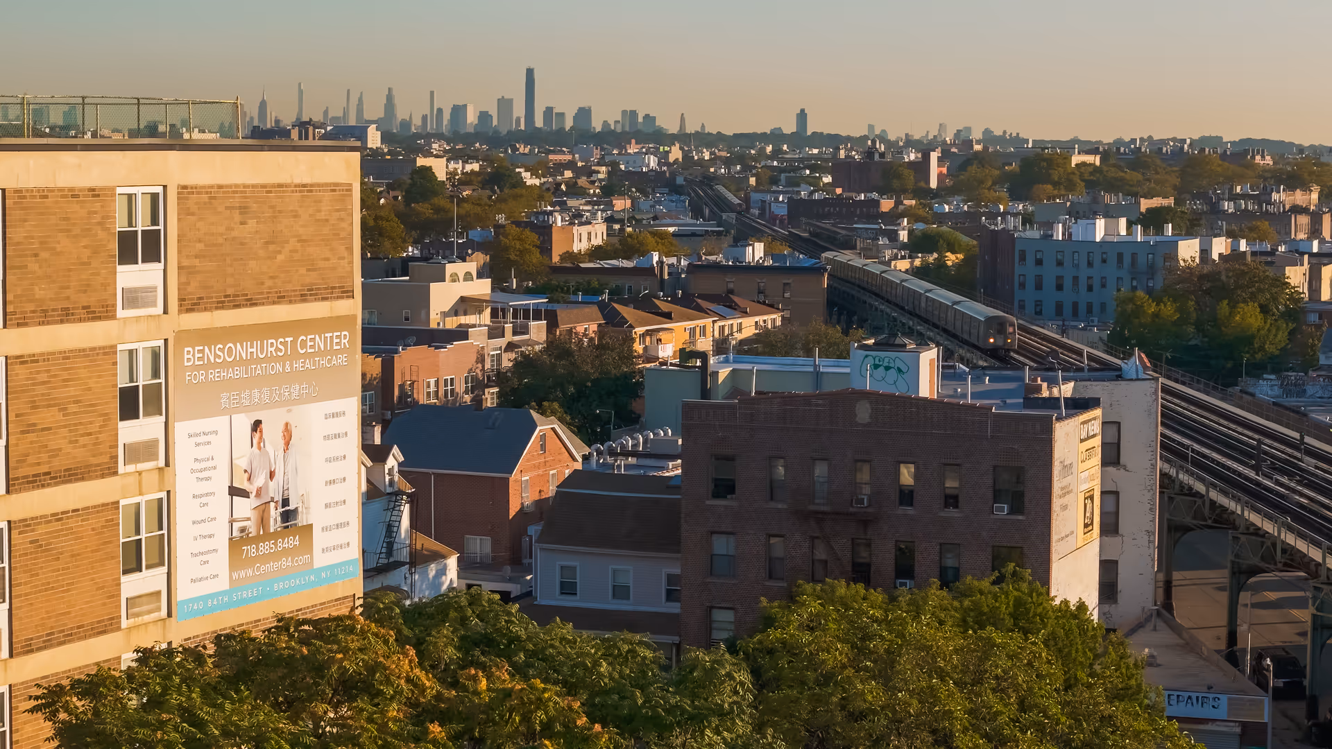 Aerial view of Bensonhurst Center building with a large exterior sign and distant city skyline.