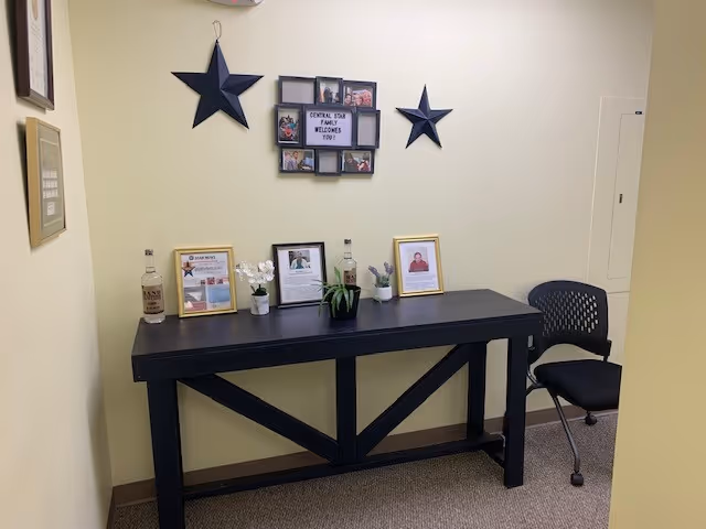 A dark wooden reception desk with framed photos and a chair against a pale wall.