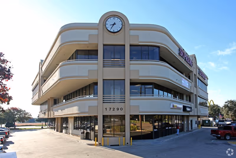 Three-story beige commercial building with a central clock tower and large glass windows.