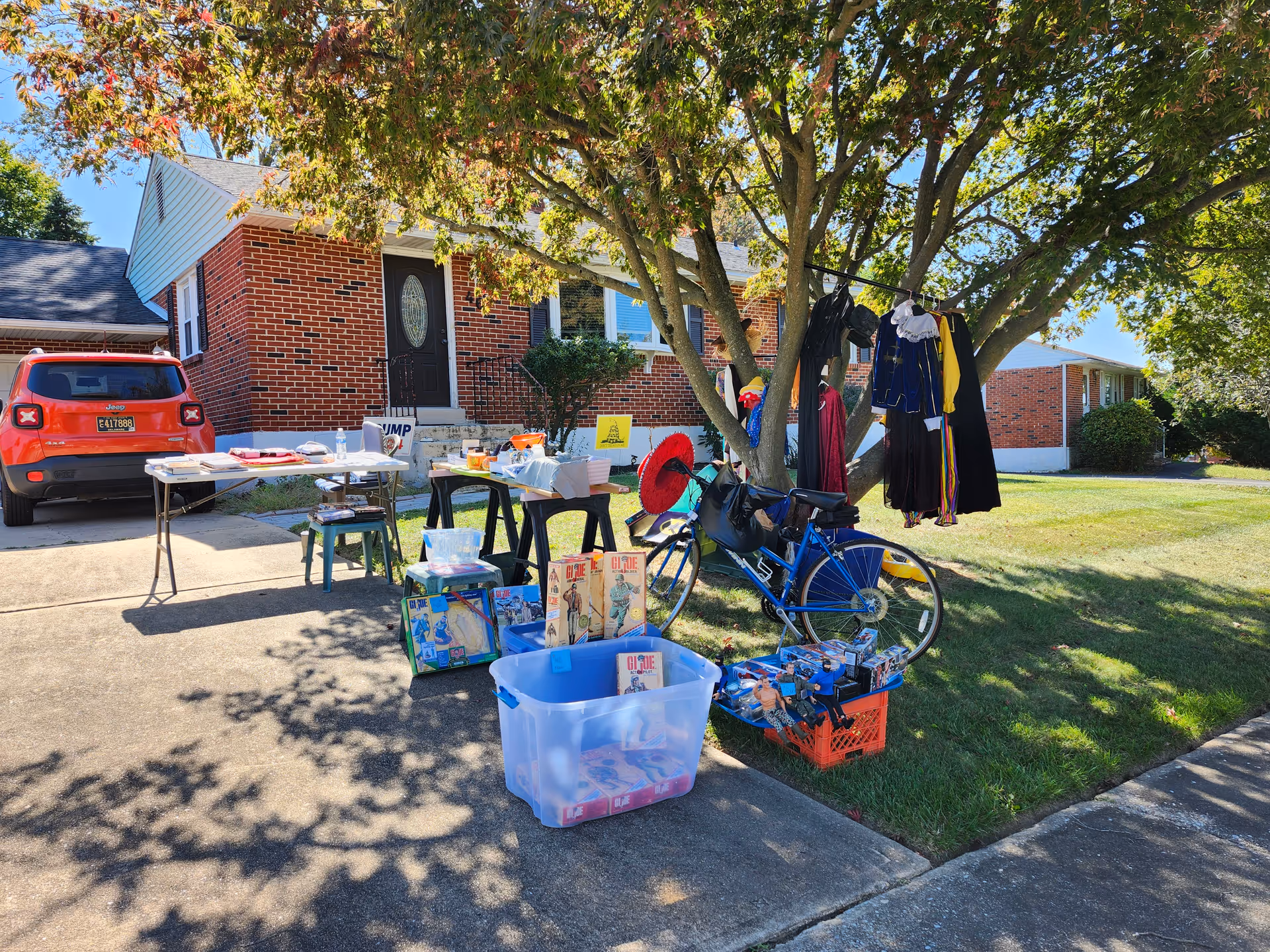 Residential front yard with sale tables, a bike, and clothes hanging on a line.