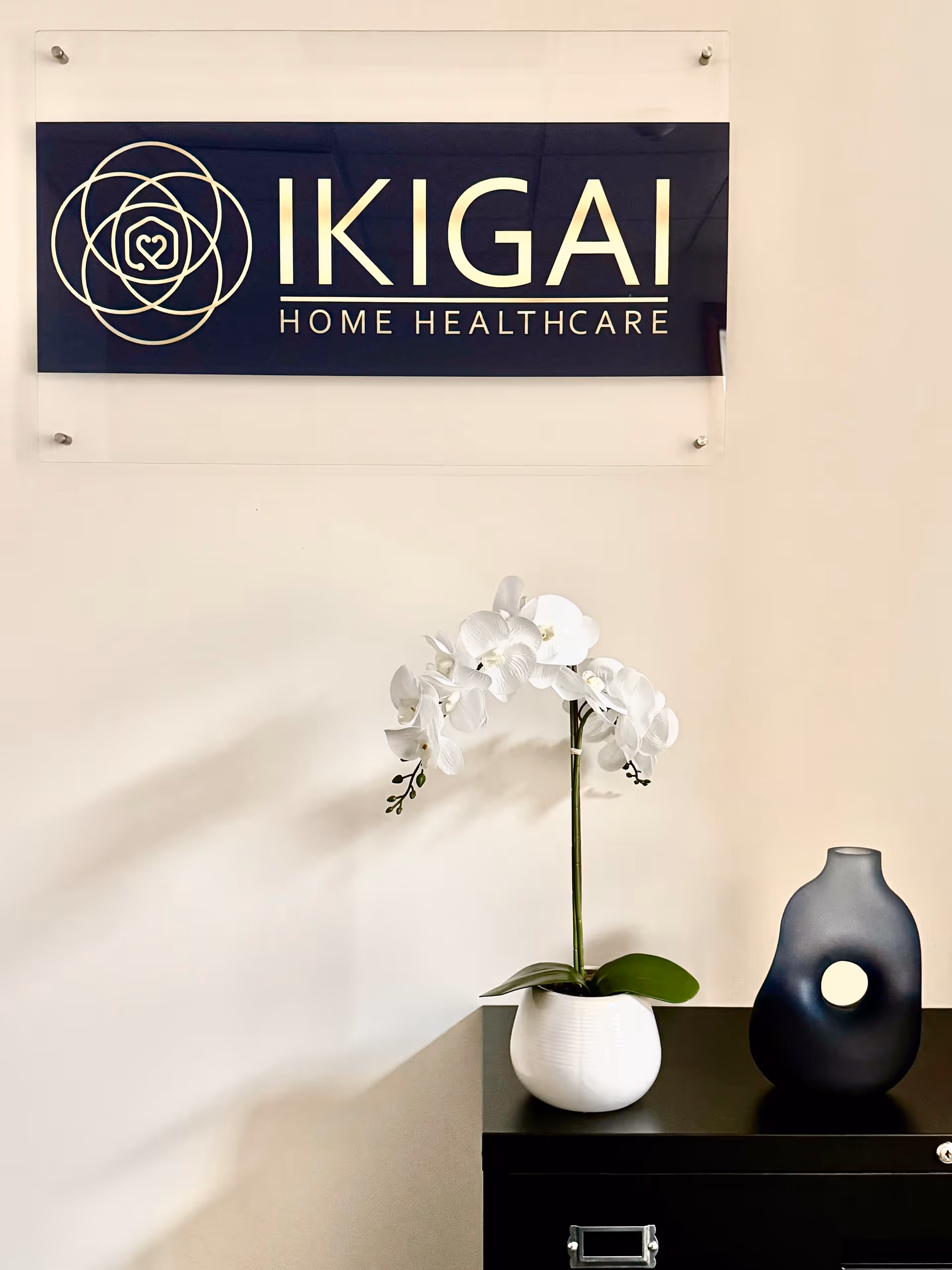Interior lobby featuring Ikigai Home Healthcare sign, white orchid, and dark vase on a cabinet.