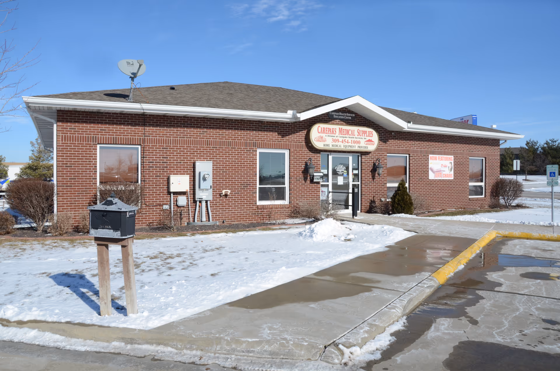 Brick building front with Carepaks Medical Supplies sign, snow, and a small parking area.