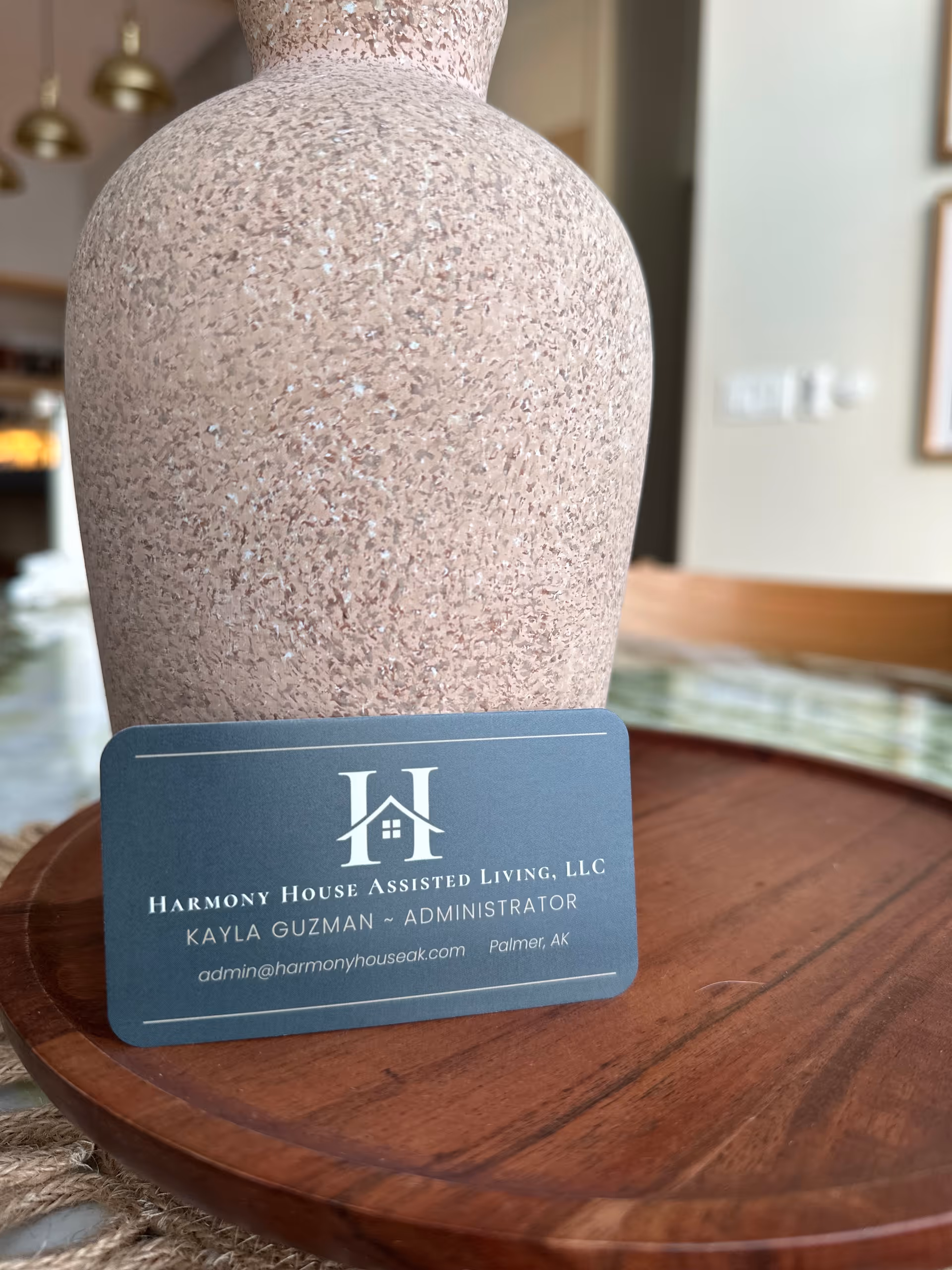 Close-up of a speckled vase and Harmony House business card on a wooden table.
