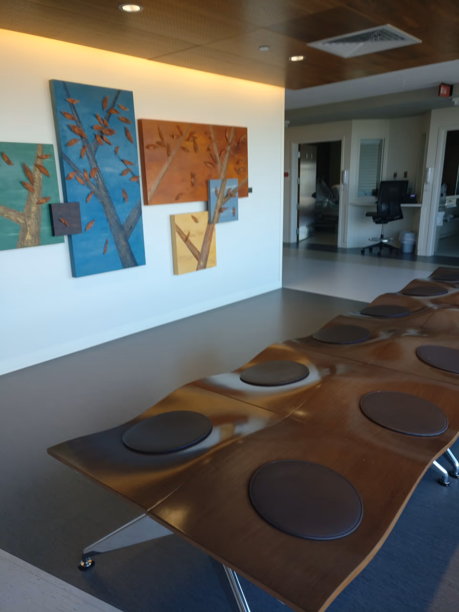 Long wooden table with round black pads in a modern facility lobby.