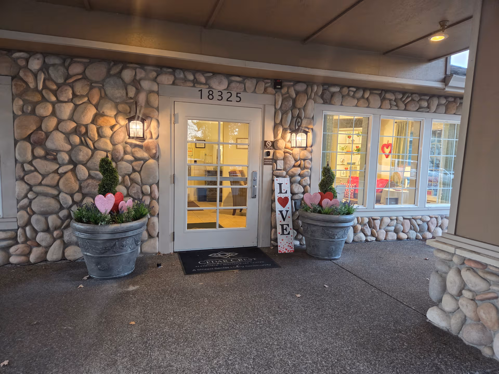 Stone facade entrance with glass door, windows, and decorative planters by the doorway.