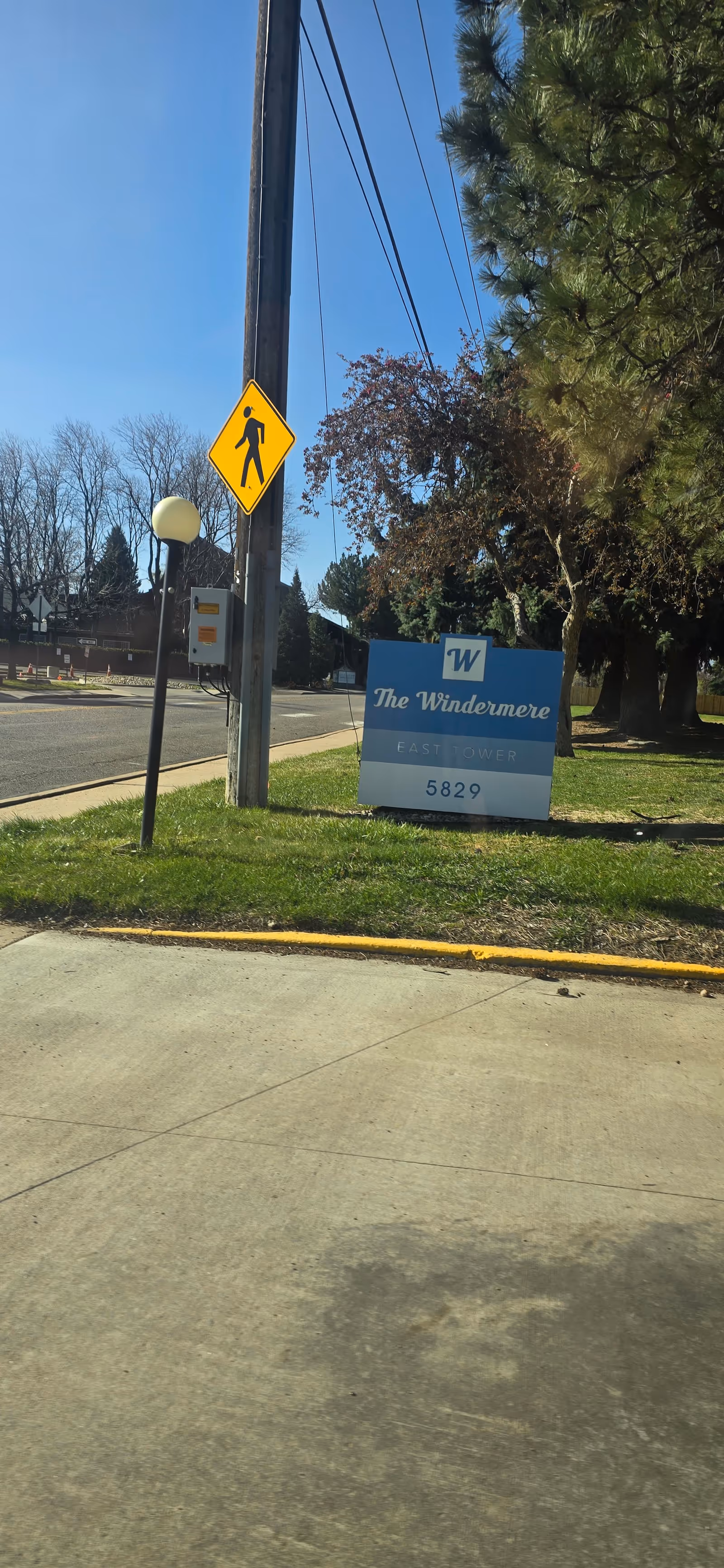 Outdoor view of The Windermere facility sign beside a sidewalk and trees.