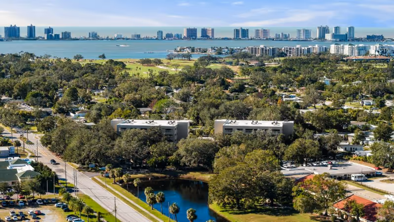 Aerial view of a Wellspring Lutheran Services campus with trees, buildings, and a distant waterway.
