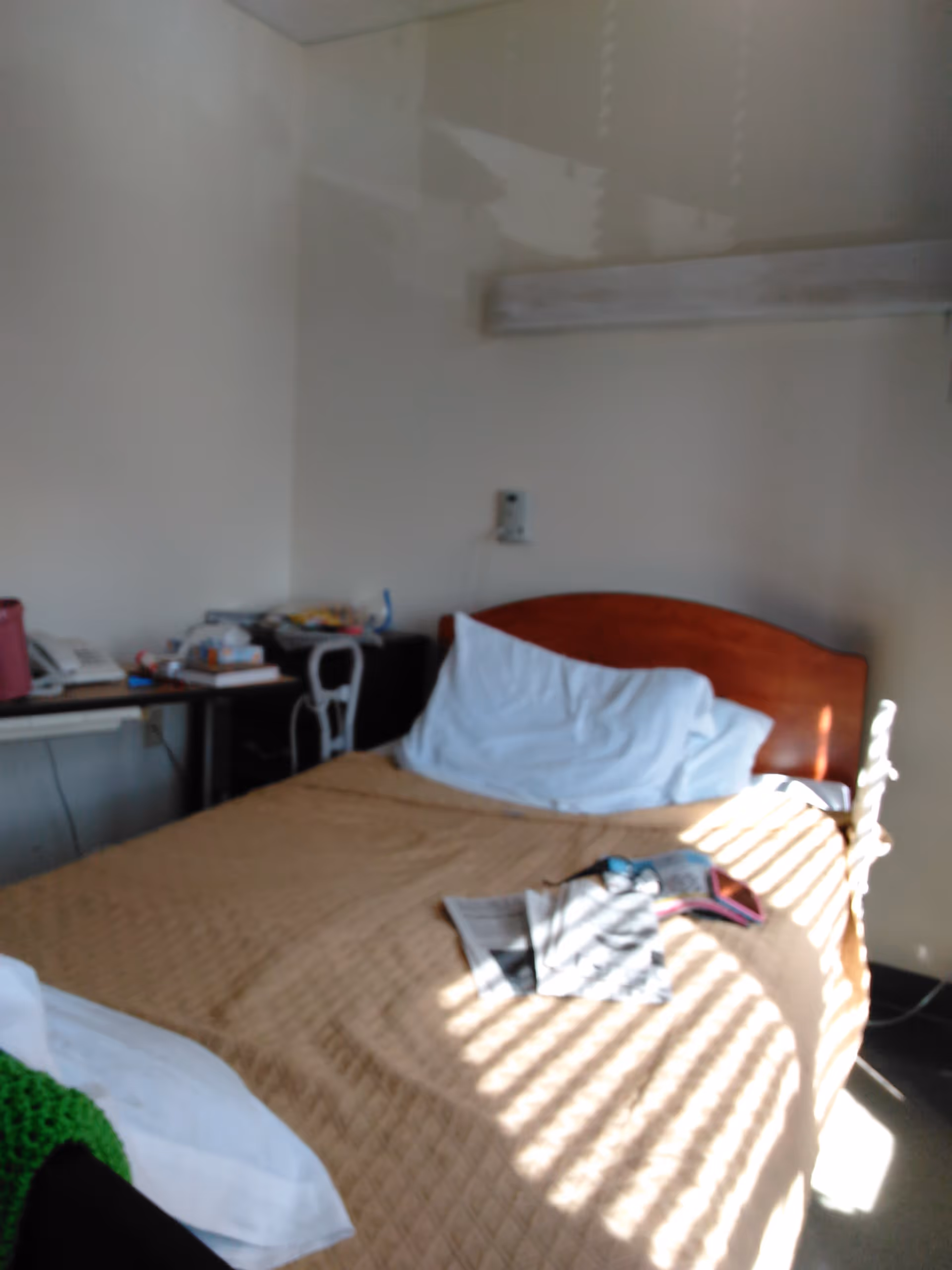 A senior living bedroom with a wooden headboard bed and cluttered desk.
