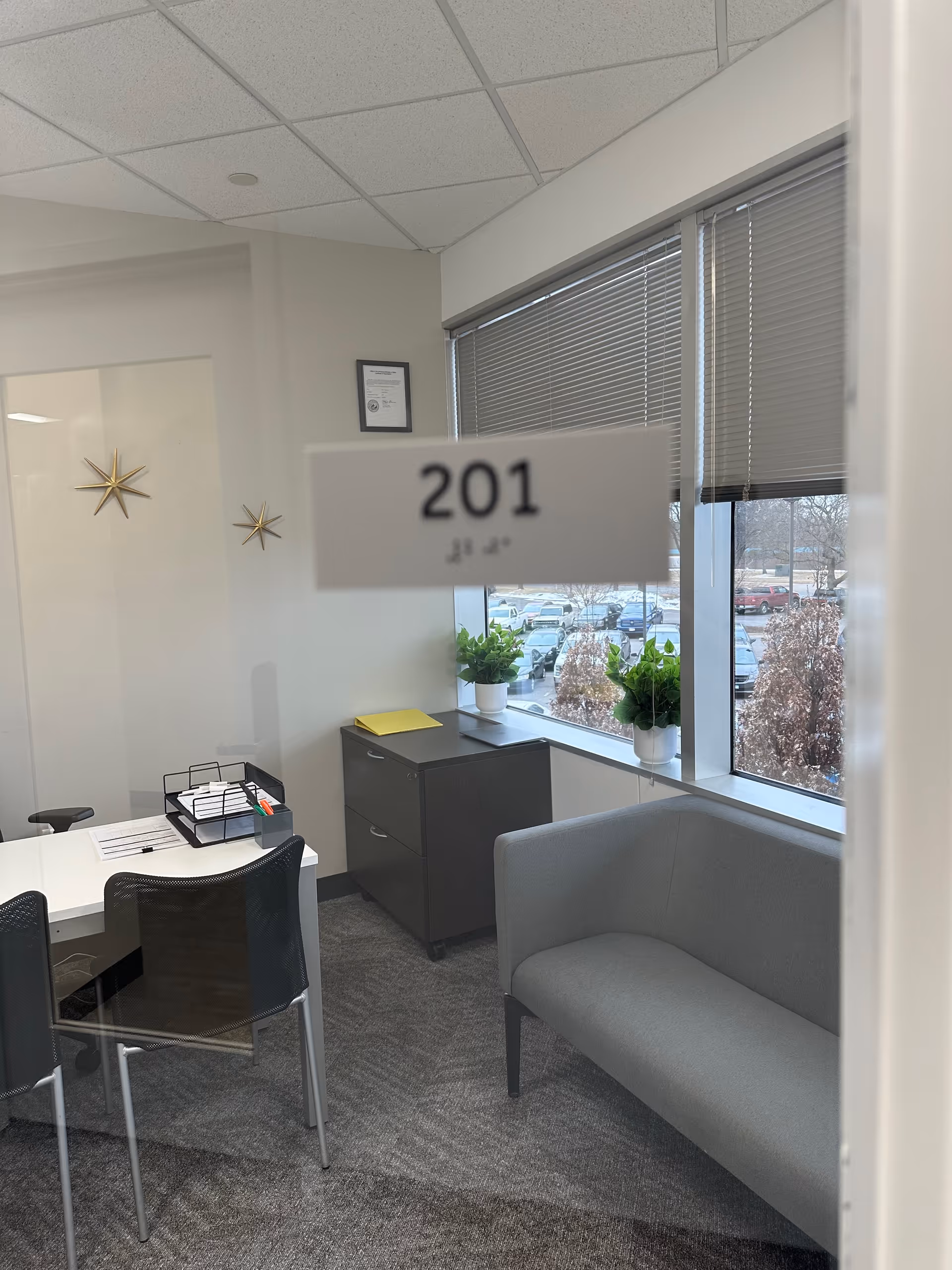 Office-style reception area with 201 room sign, desk, chairs, cabinet, sofa, and windows.