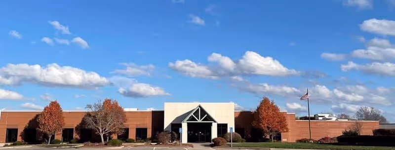 Wide view of a brick building front with a glass entry and flagpole.