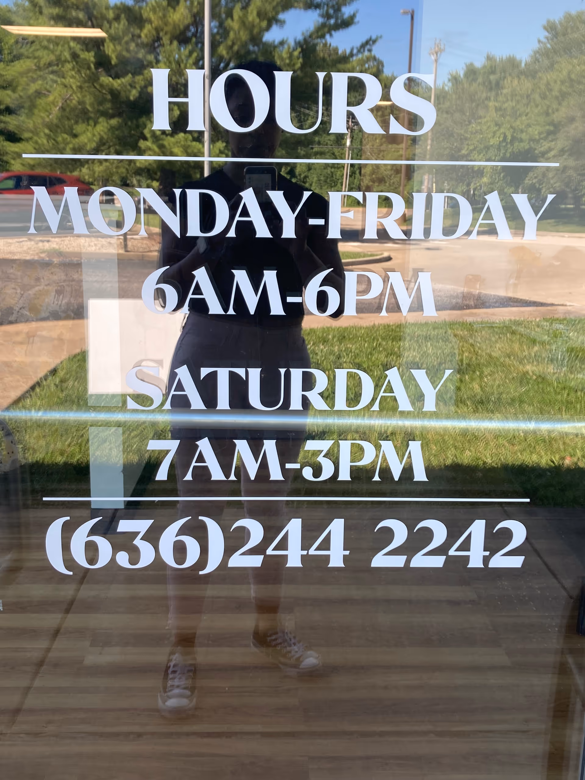 Glass entrance door displays hours and phone number; photographer's reflection visible.