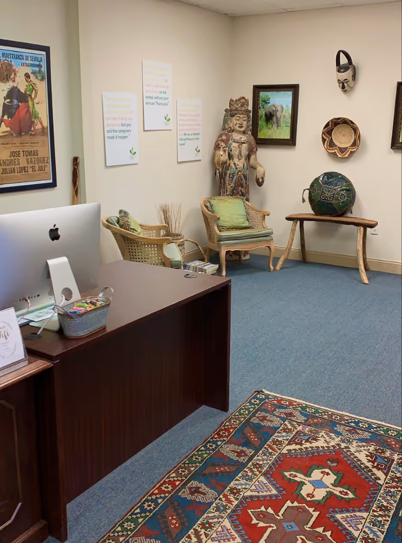 A reception area features a dark wood desk, computer, chairs, rug, and cultural artwork.