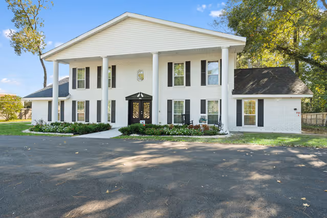 White brick senior living facility with tall columns and a paved driveway.