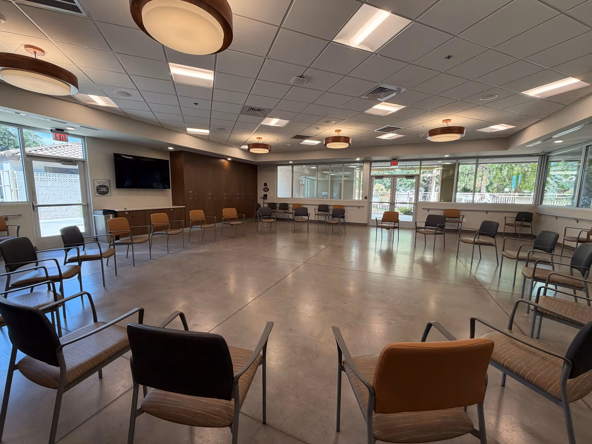 Spacious interior room with a circular arrangement of chairs, windows, and a wall-mounted TV.