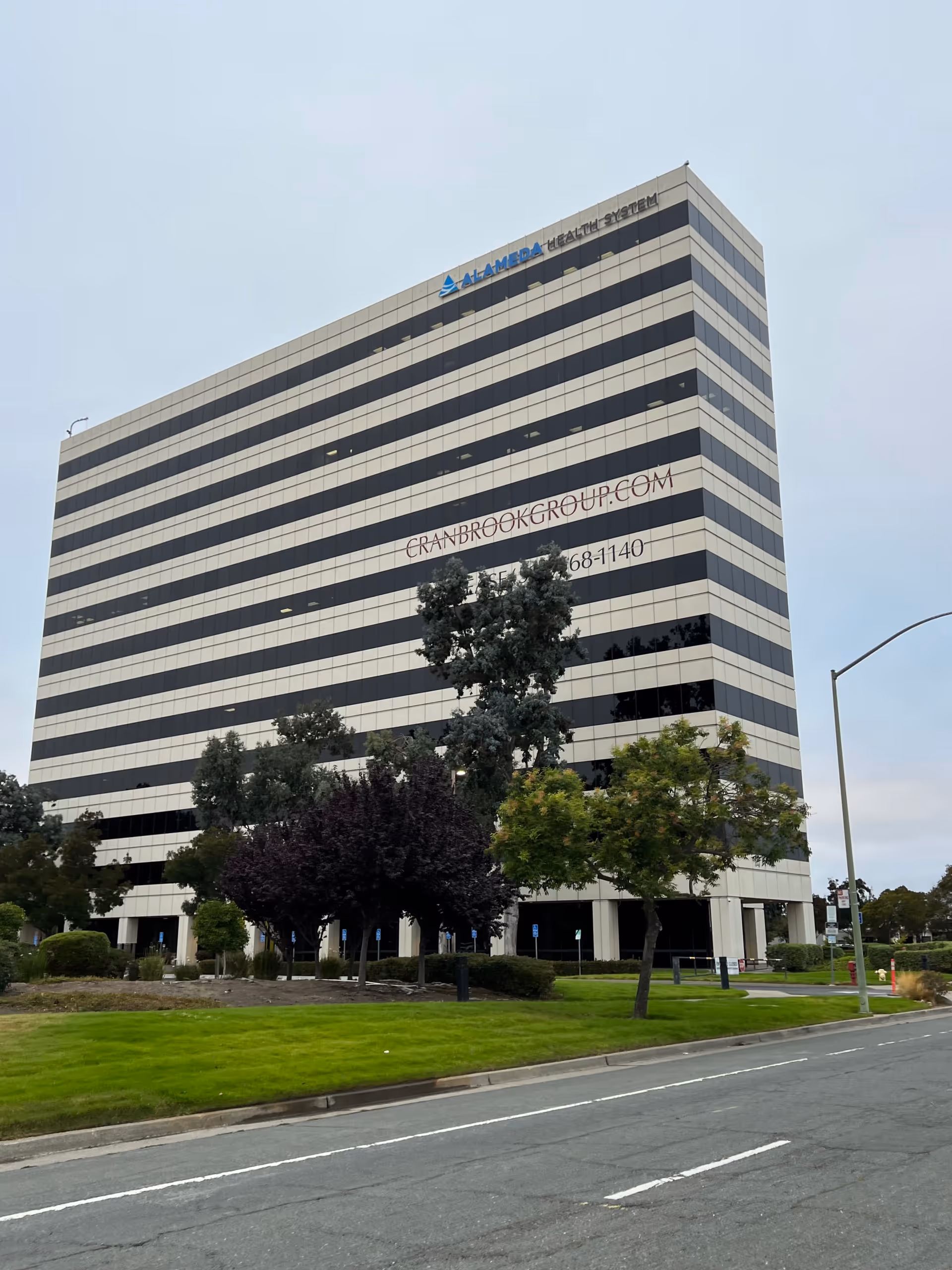 Tall striped office building with trees and a street in foreground.