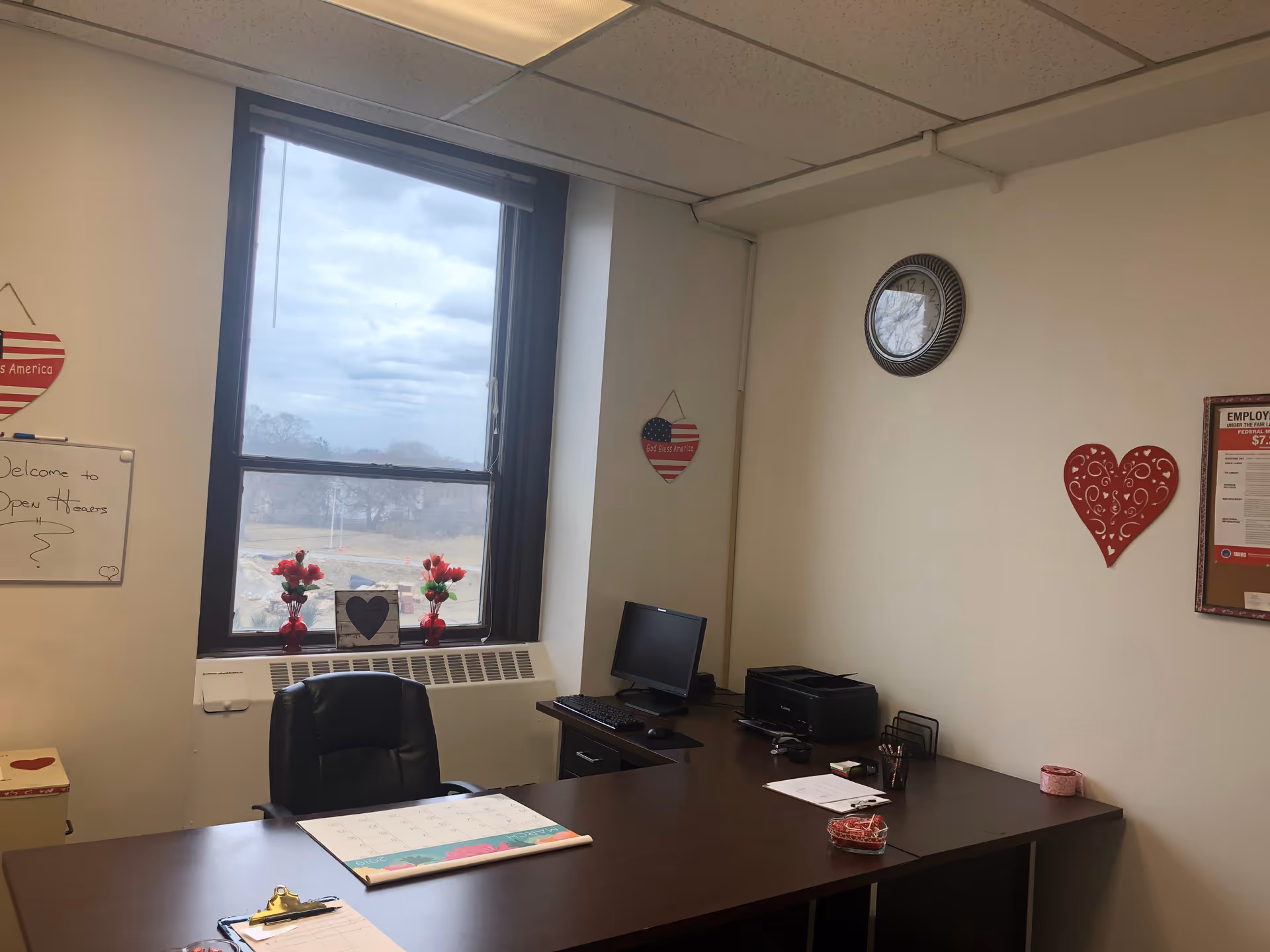 Office workspace with desk, computer, printer, window, and red heart decorations.