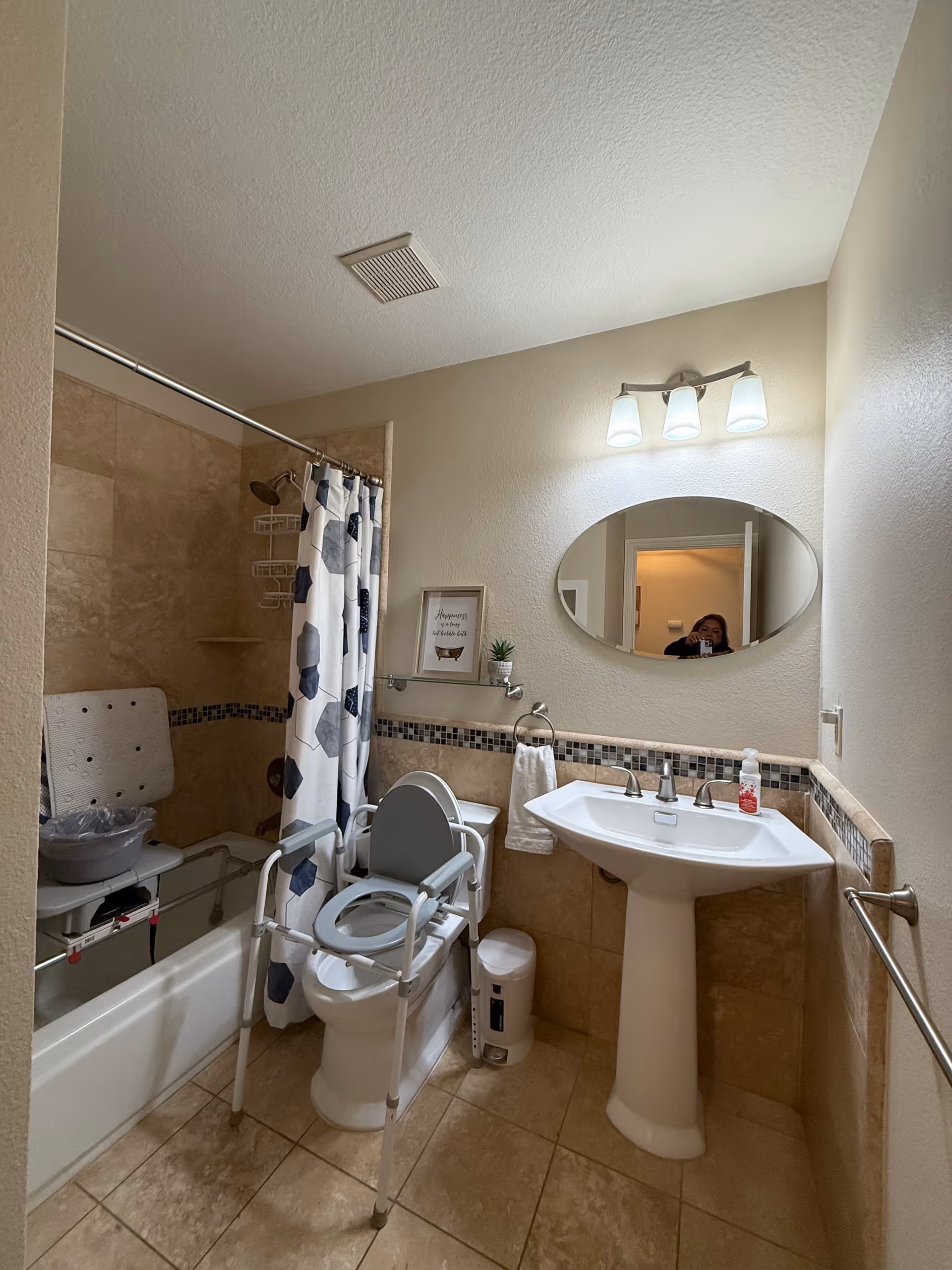 Accessible bathroom featuring a tub/shower, raised toilet seat, sink, and mirror.