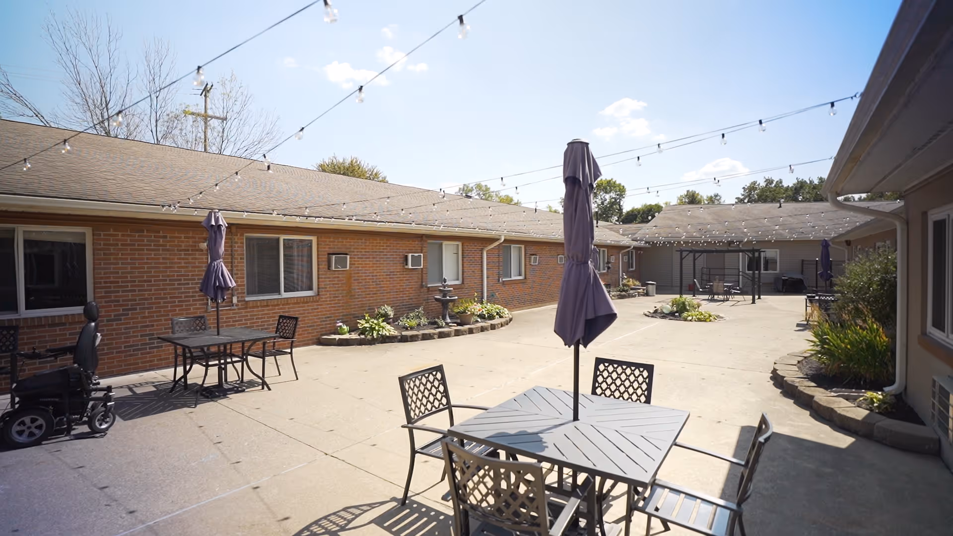 Outdoor courtyard at Ambassador Healthcare with string lights, tables, chairs, and planters.