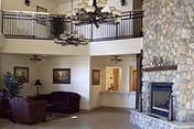 A spacious senior living lounge with a stone fireplace, comfy seating, and a second-floor balcony.