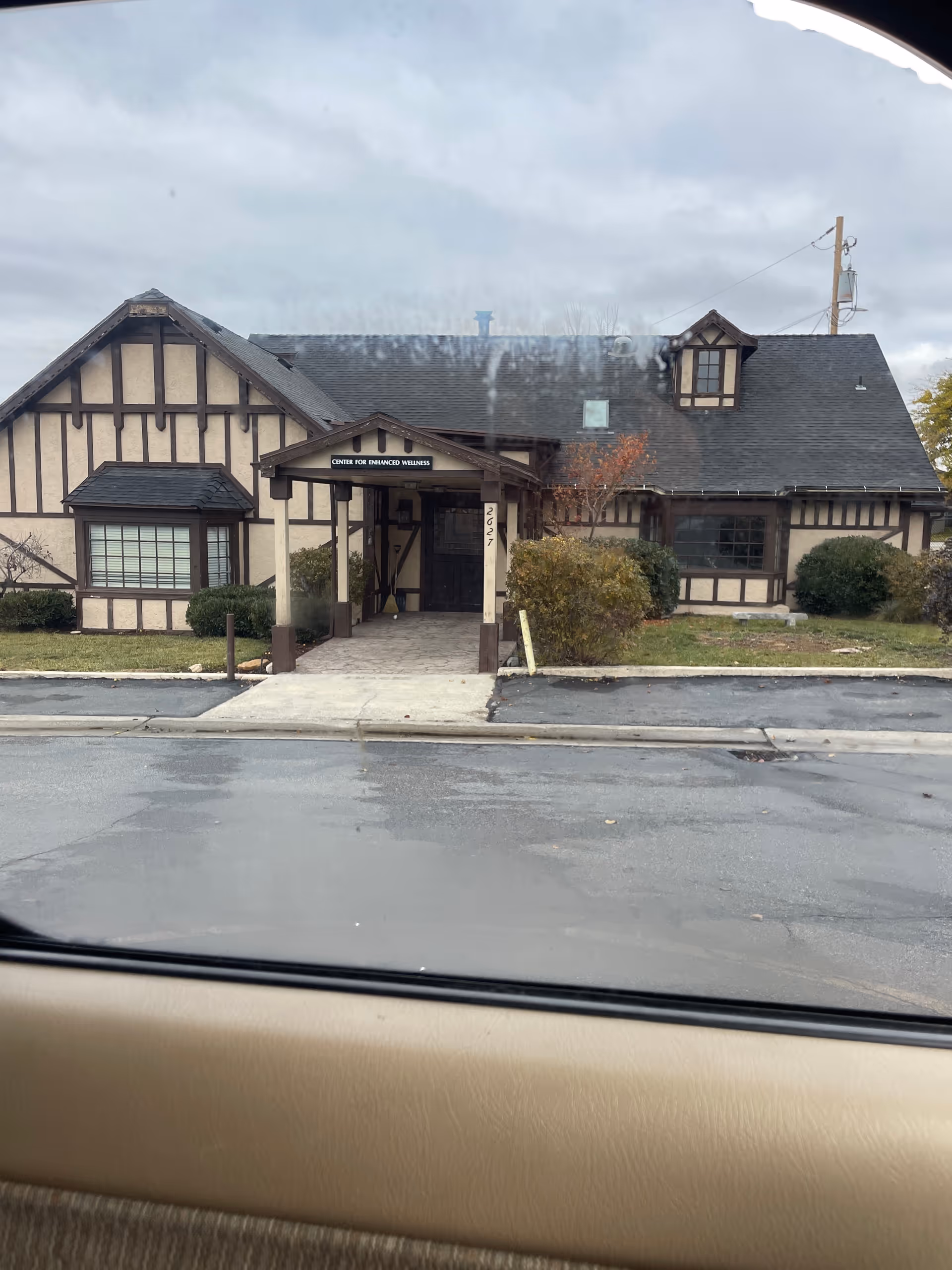 Exterior of Tudor-style facility with a covered entrance, shrubs, and a parking lot.