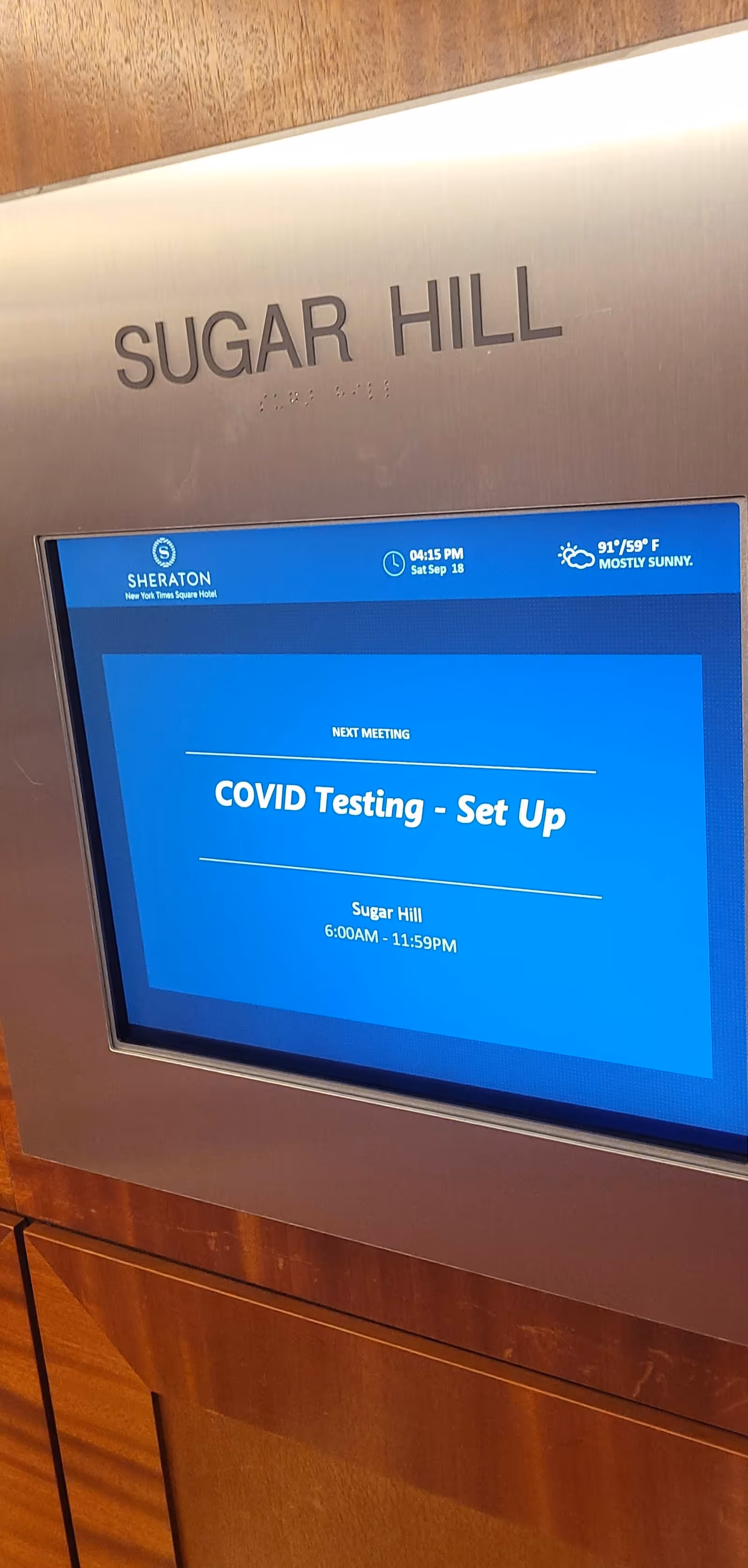 Metal wall panel with 'SUGAR HILL' sign and blue COVID testing display