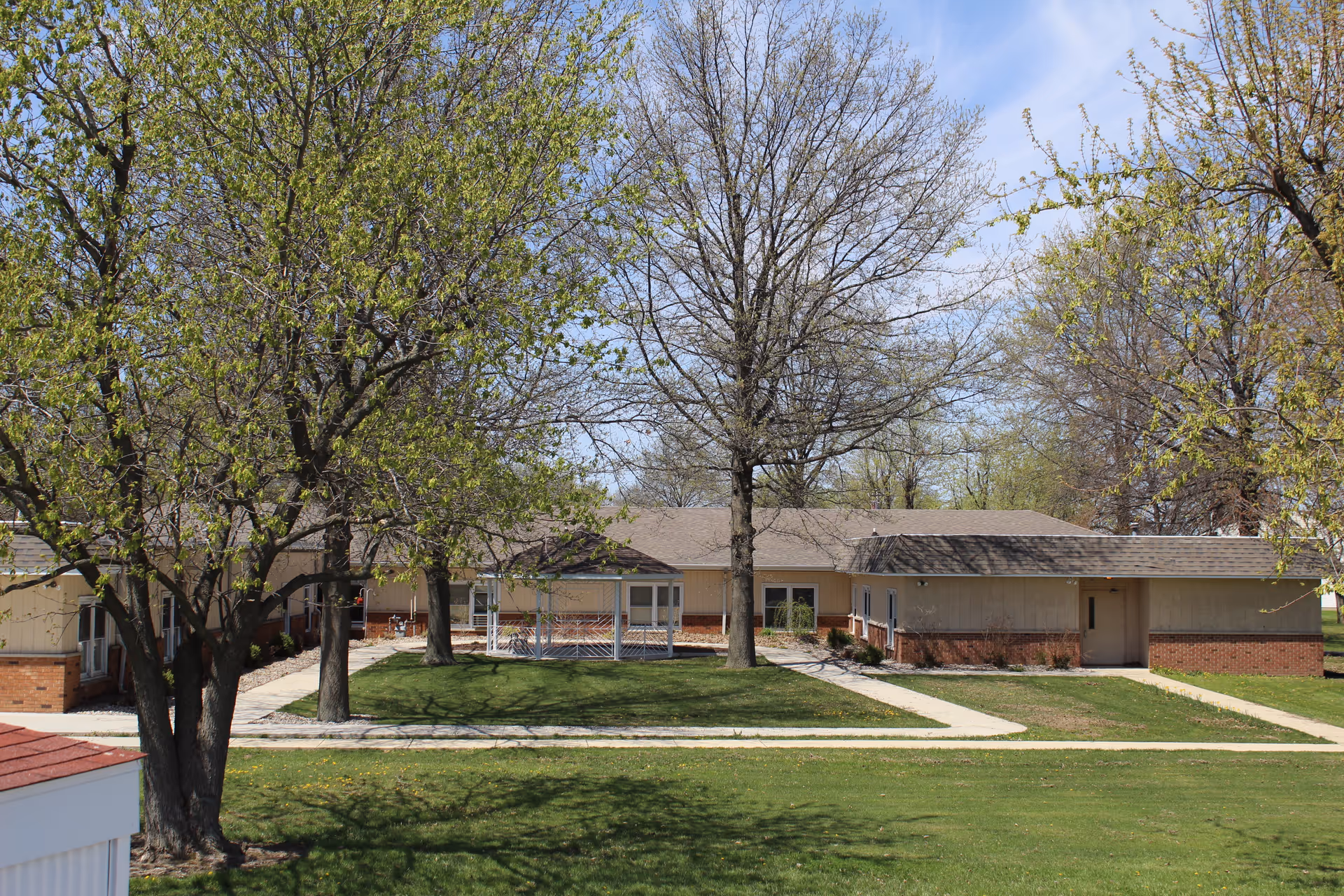 Single-story care facility building with a grassy lawn, trees, and paved walkways in front.