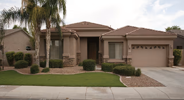 Single-story tan residence with a two-car garage, palm trees, and landscaped front yard.