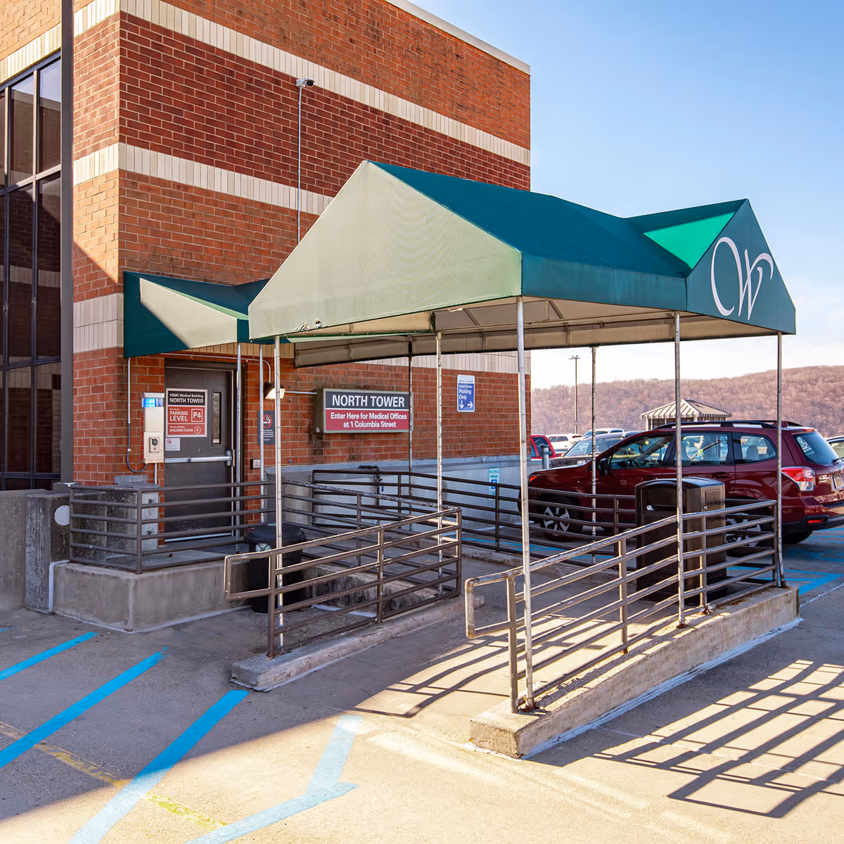 Brick medical building entrance with a green canopy and wheelchair ramp.
