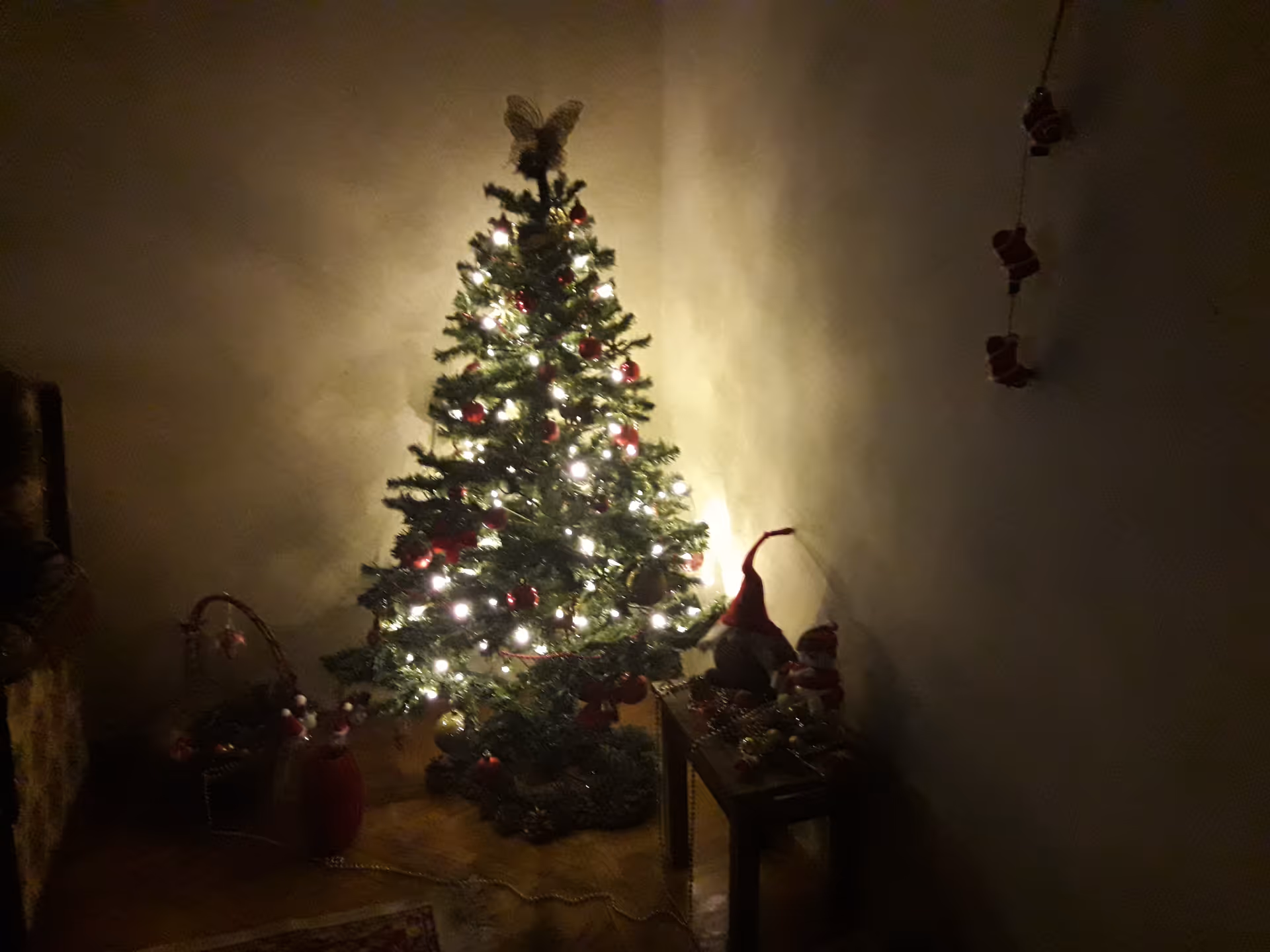 Dimly lit interior corner with a decorated Christmas tree and festive decorations.