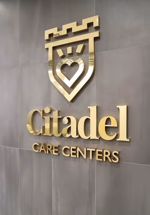 Gold Citadel Care Centers logo and sign mounted on a gray wall.