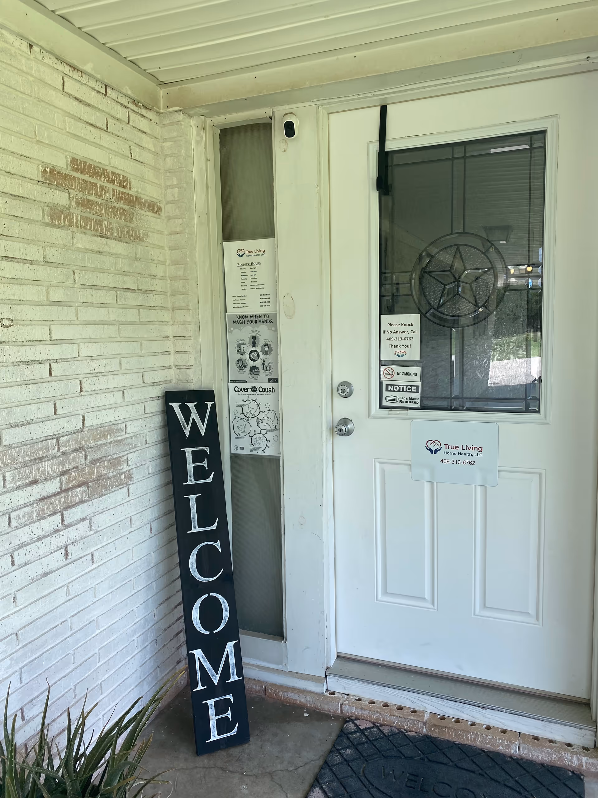 Exterior entrance with a white door, welcome sign, and posted notices at a senior care facility.