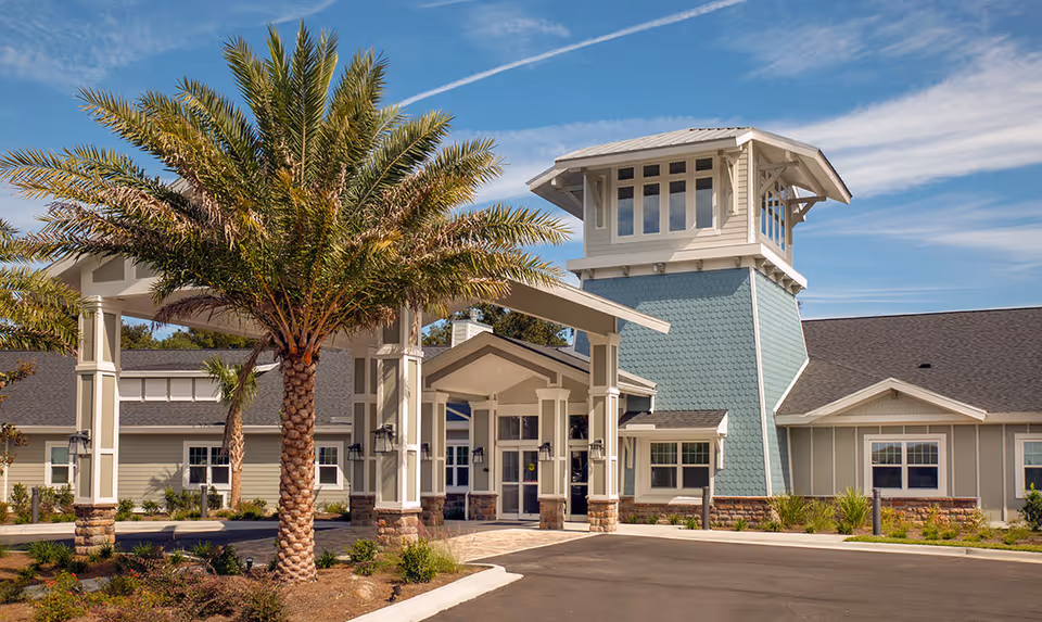 Modern senior living facility exterior with palm trees and a covered front entrance.