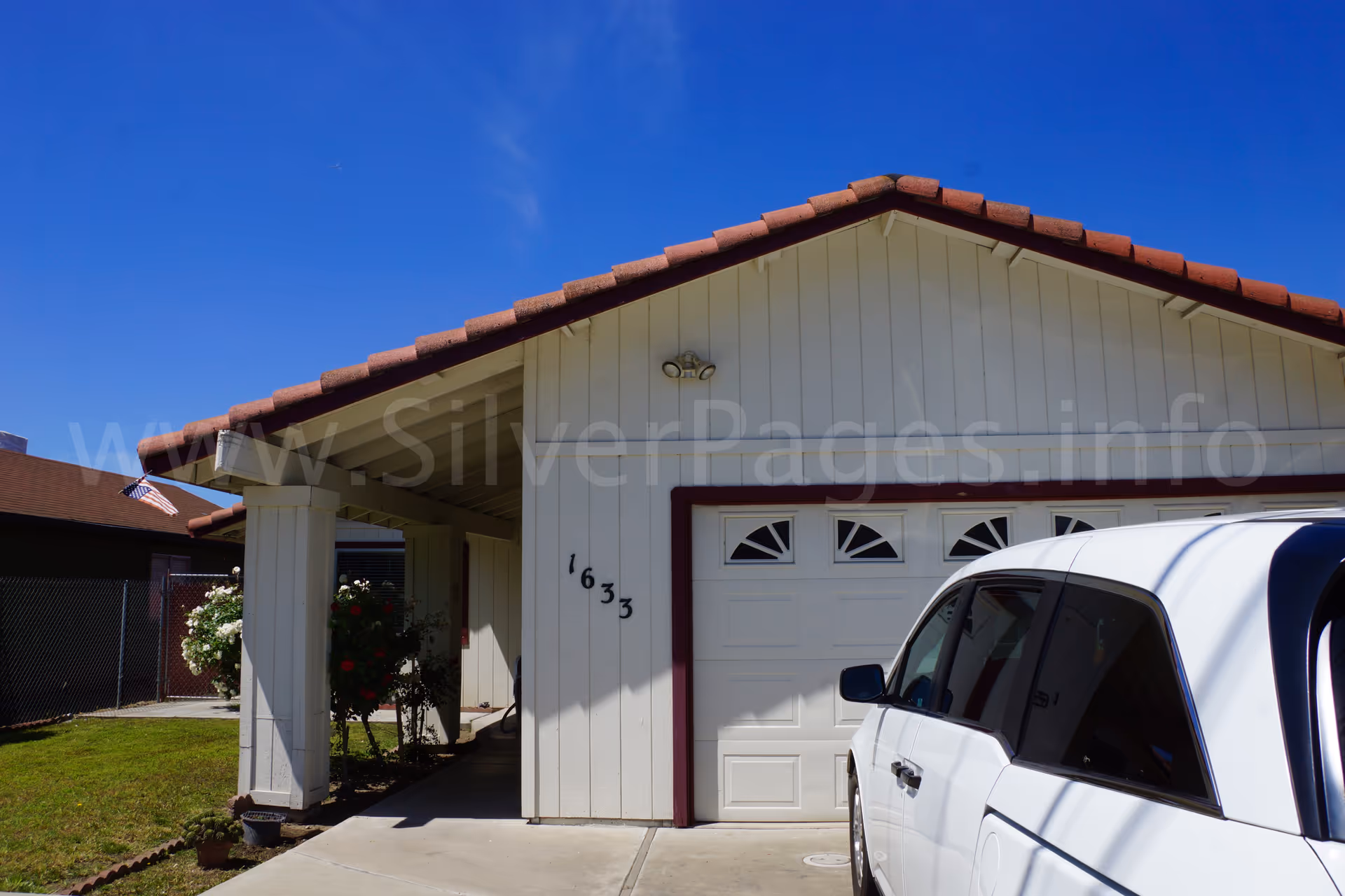 Residential-style senior living facility exterior with a white garage door, parked SUV, and green lawn.