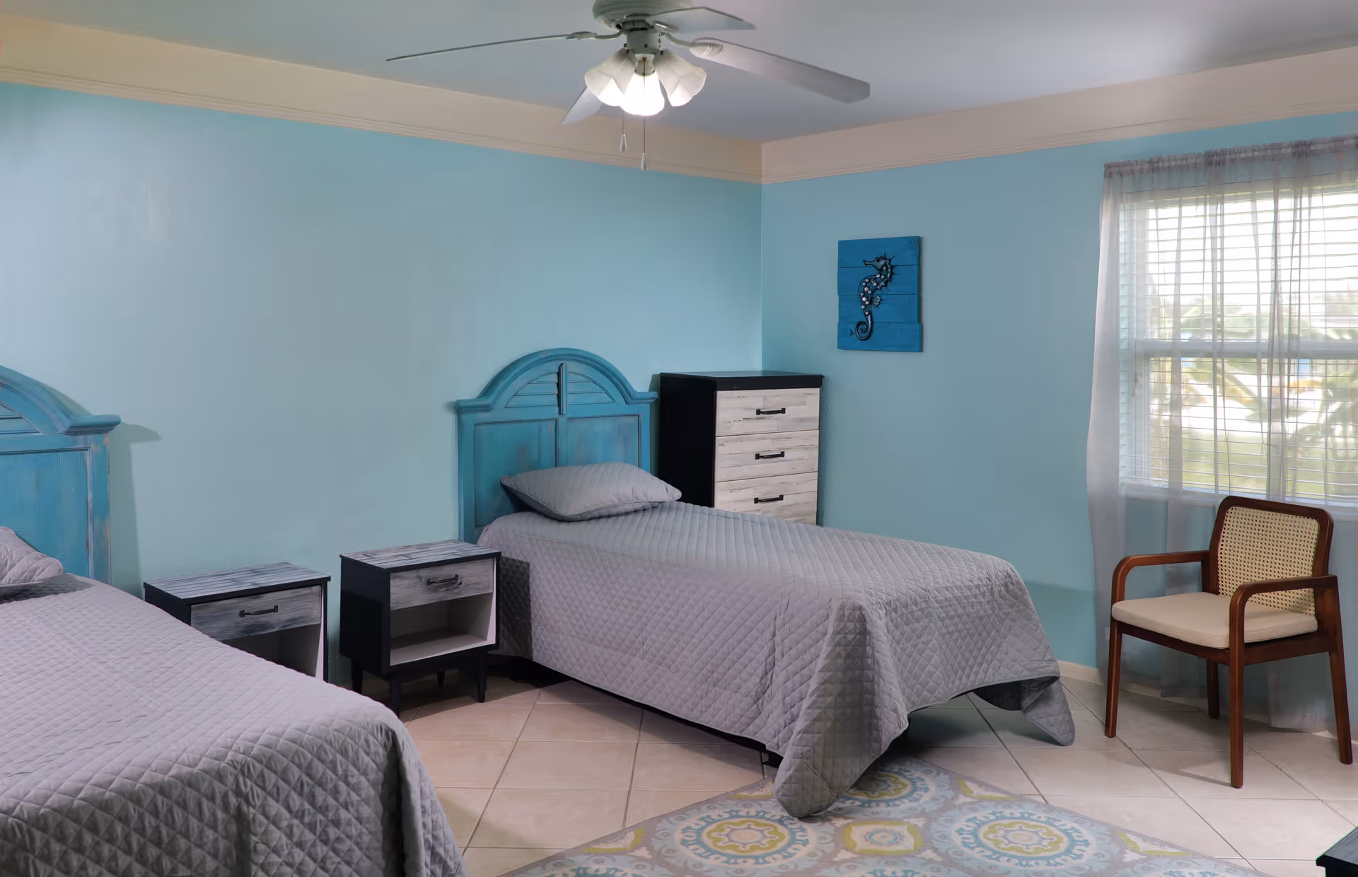 Two turquoise bedroom beds flank nightstands, a dresser, and a chair by the window.
