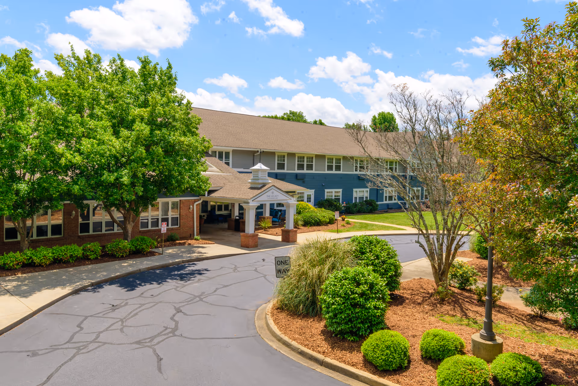 Two-story senior living building exterior with covered entrance and landscaped surroundings.