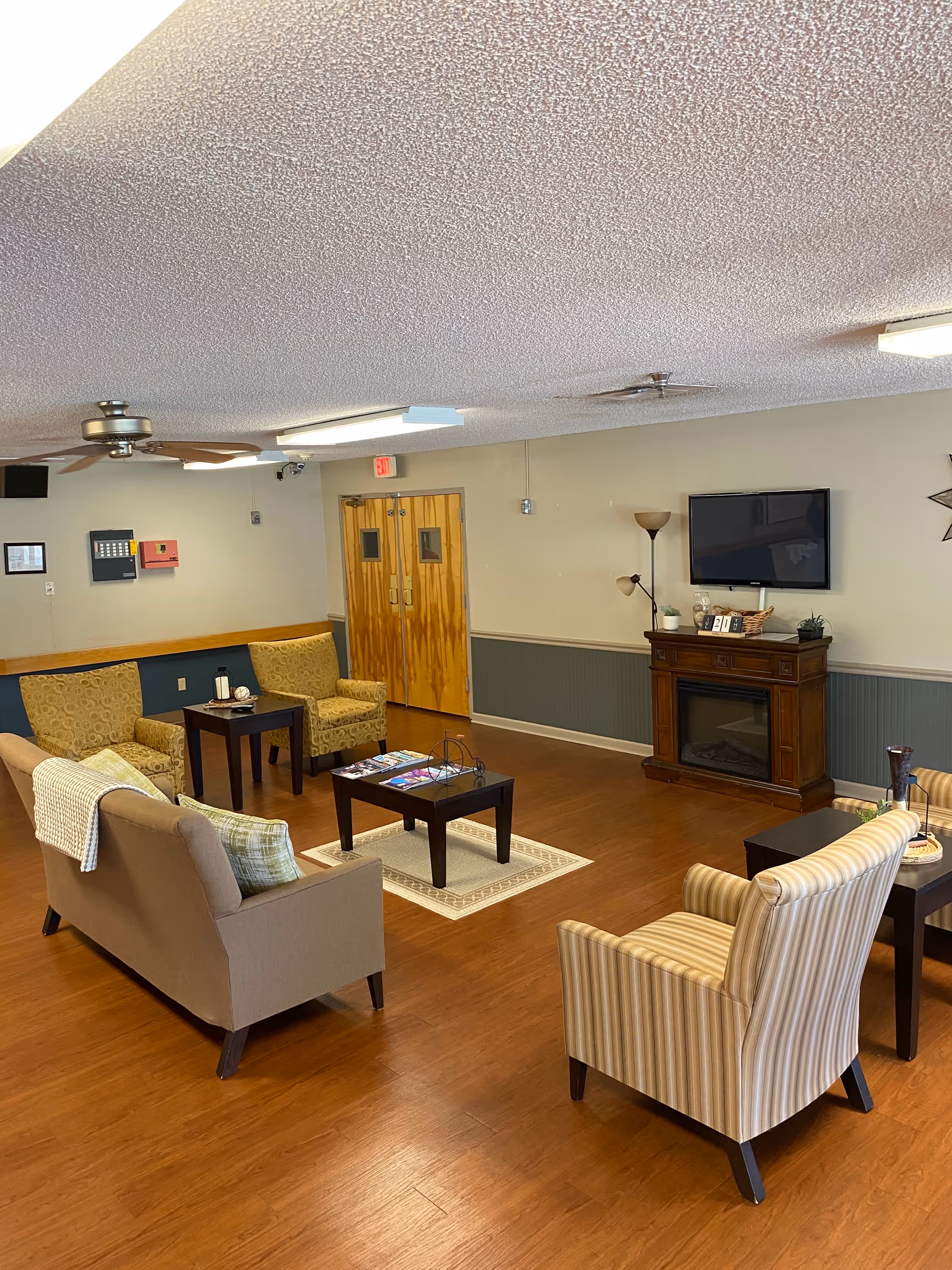 Senior living lounge with sofas, chairs, coffee tables, and a fireplace-mounted TV
