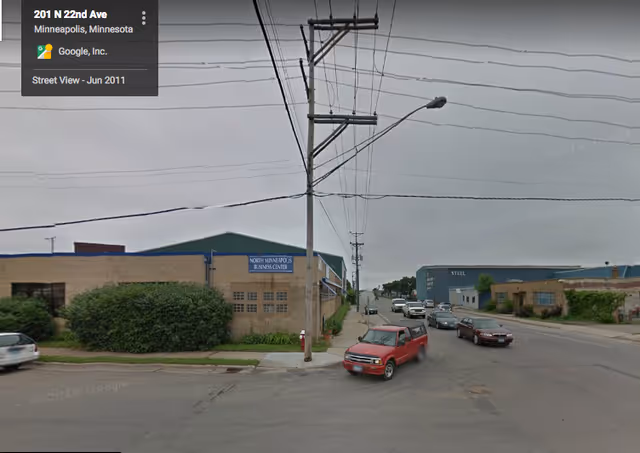 Street view of a commercial block with low brick buildings, power lines, and cars.