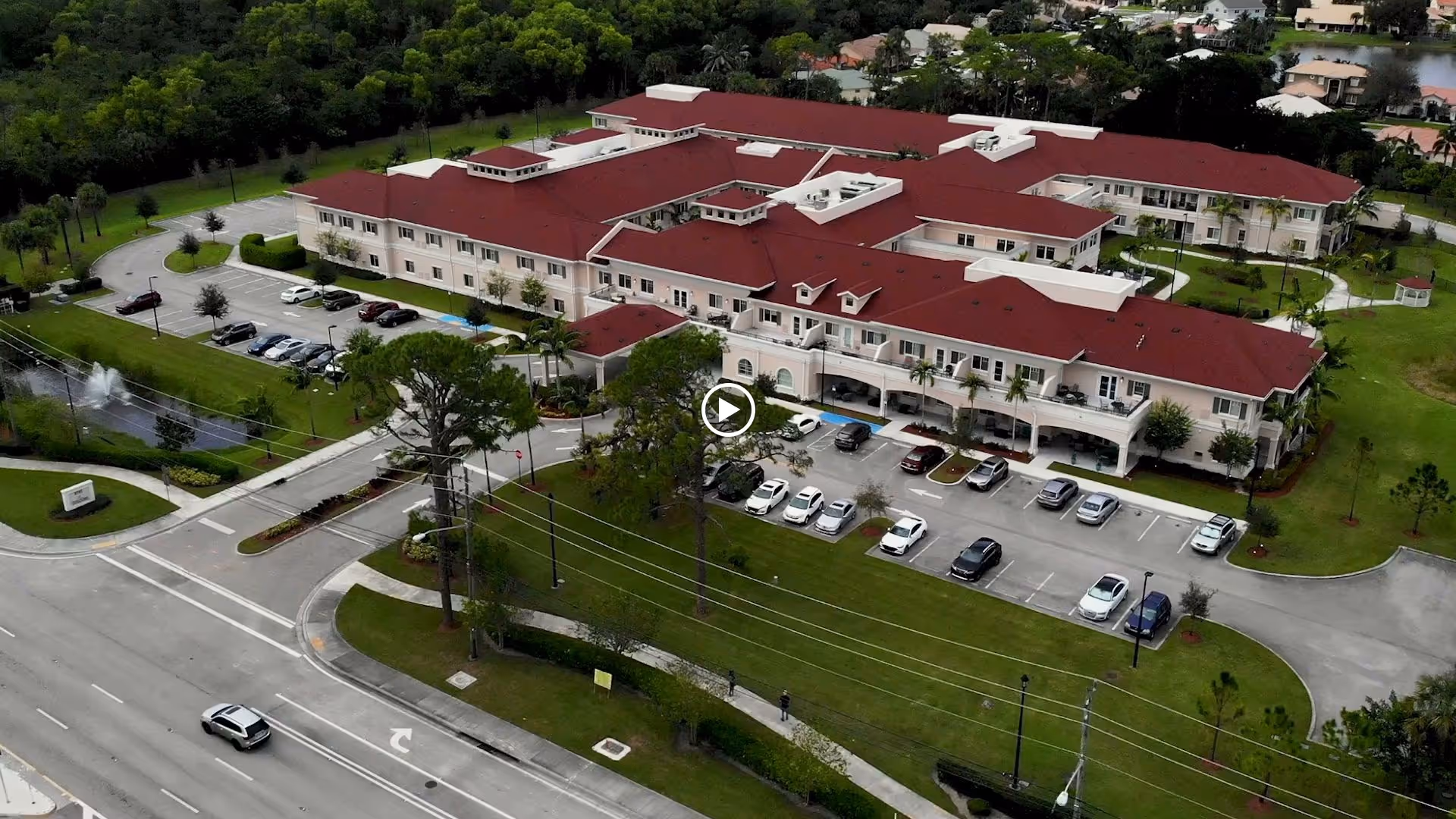 Aerial view of Alamar Senior Living’s large two-story building with red roofs, a front parking lot, pond fountain, and landscaped lawns.