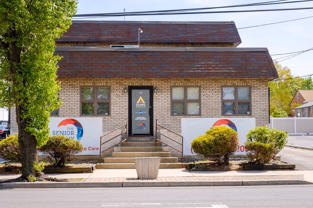 Brick building front with central door, steps, and banners announcing The Senior Company care facility.