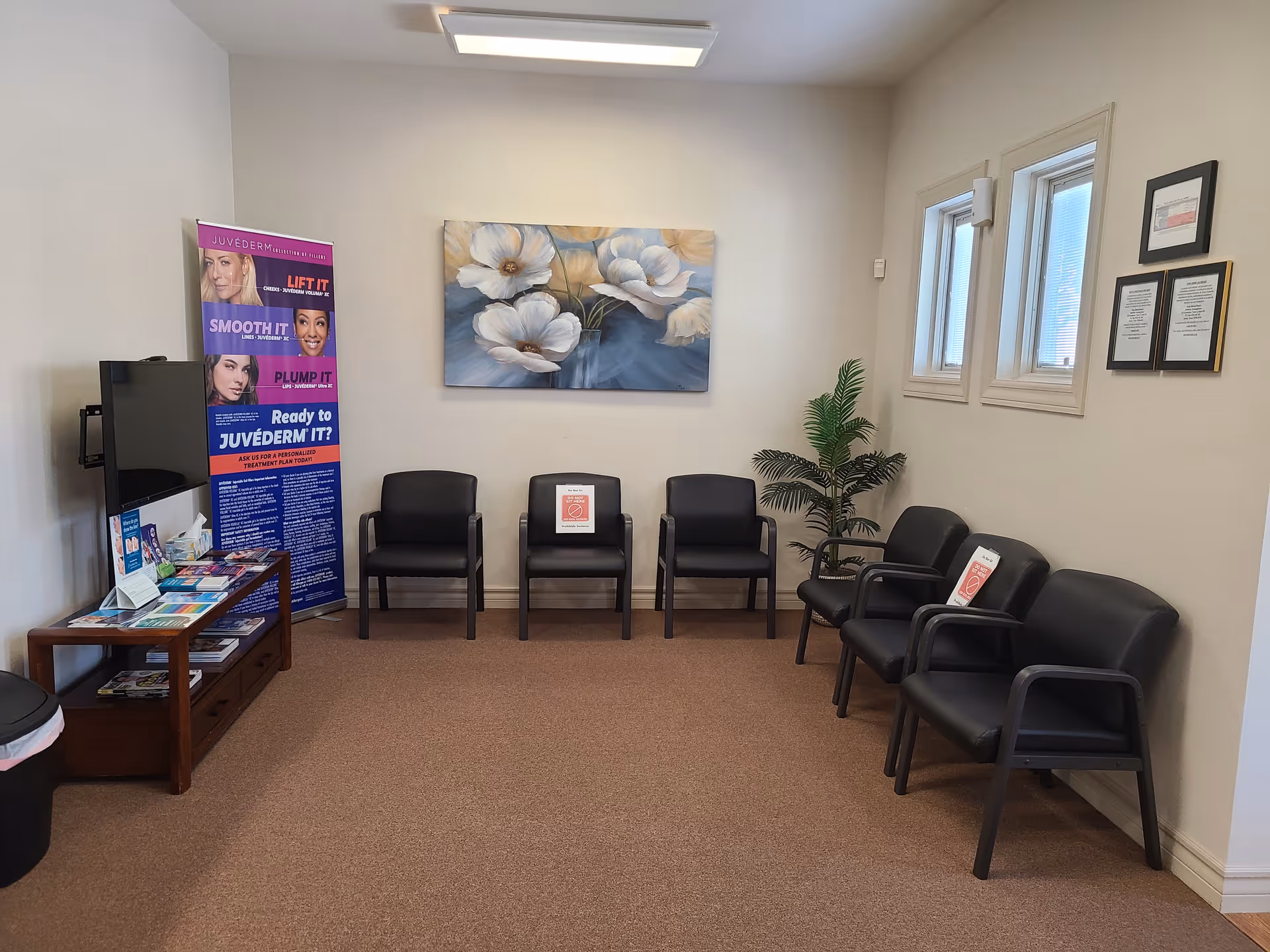 Clinic waiting area with black chairs, magazines, a plant, and wall artwork