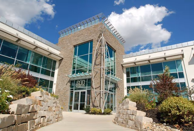 Modern senior living facility exterior with stone accents and large glass entrance under blue sky.