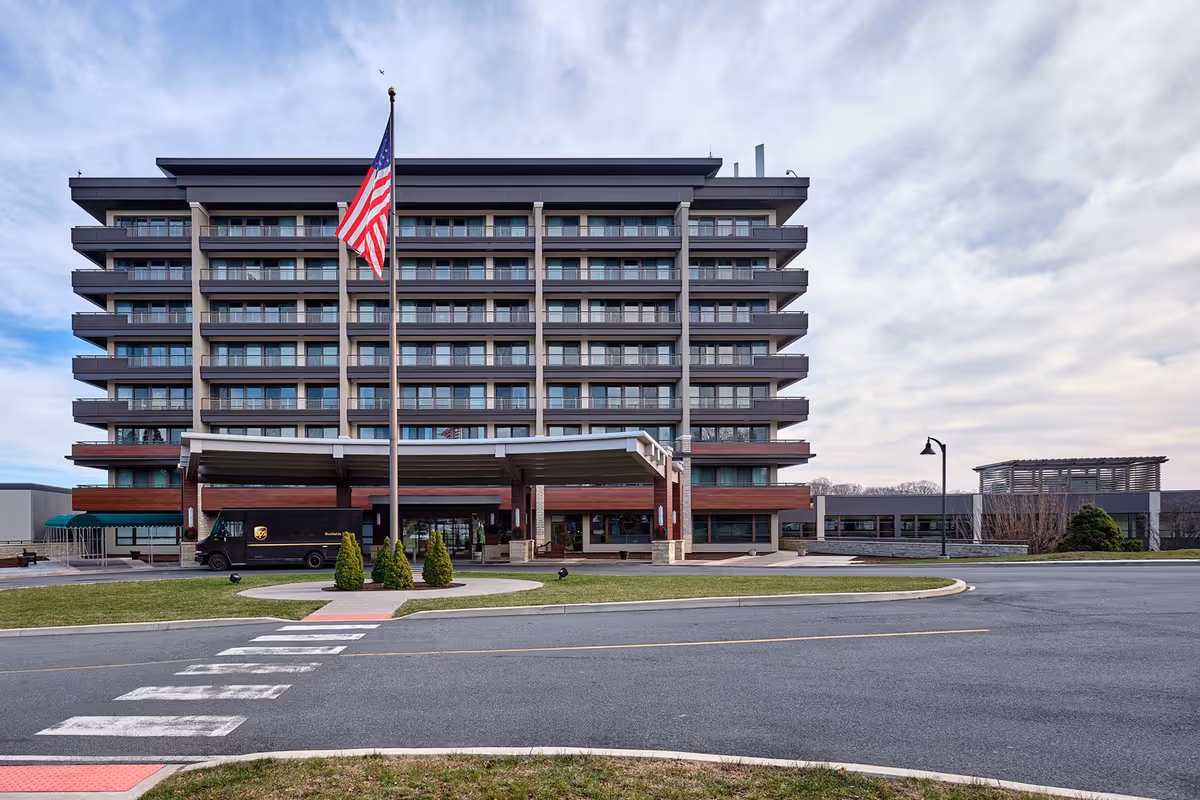 Front view of a multi-story senior living building with an American flag in front and a covered entrance.