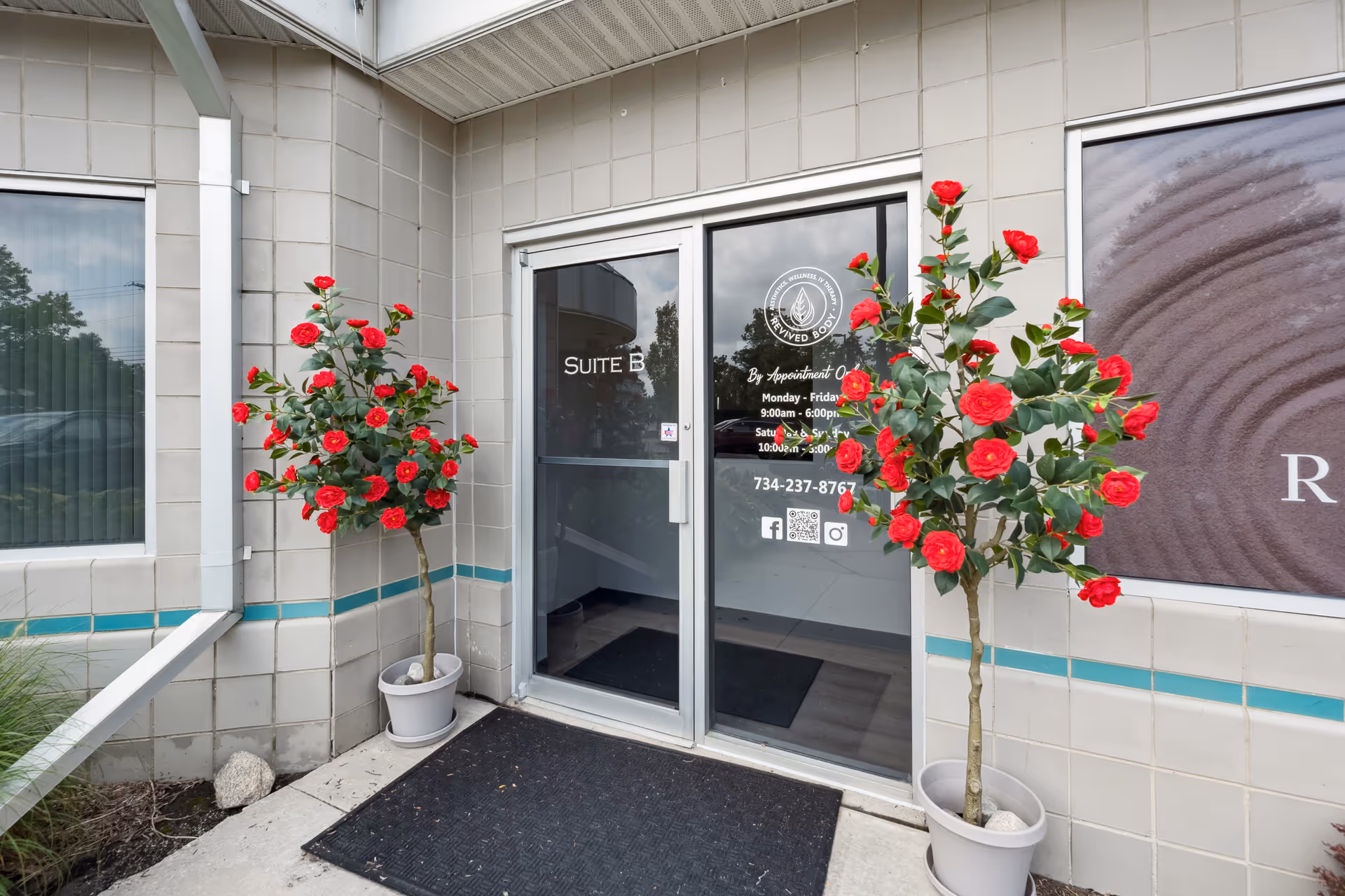 Exterior building entrance with glass doors and red potted roses on each side.