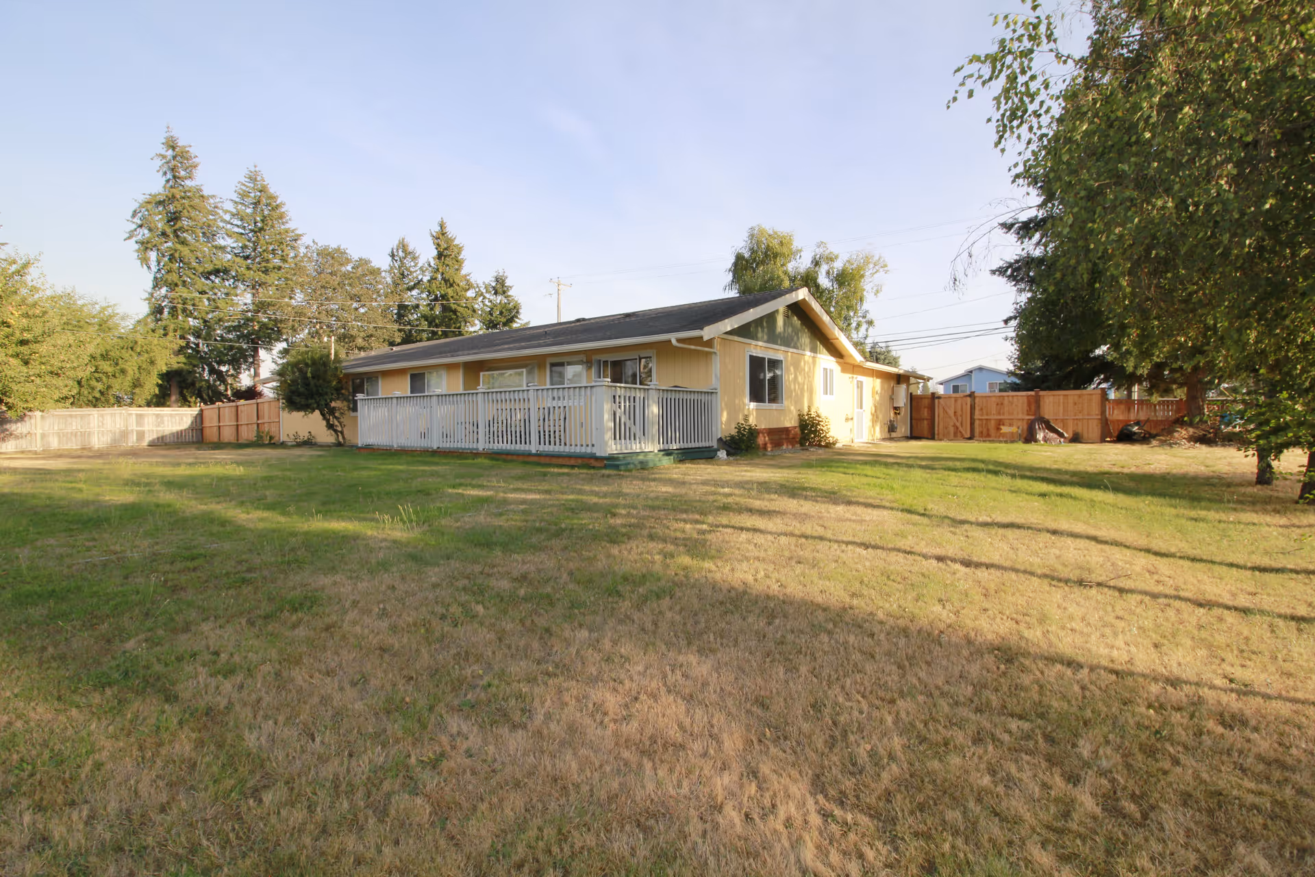 Single-story yellow house with white railing deck, surrounded by a grassy yard.