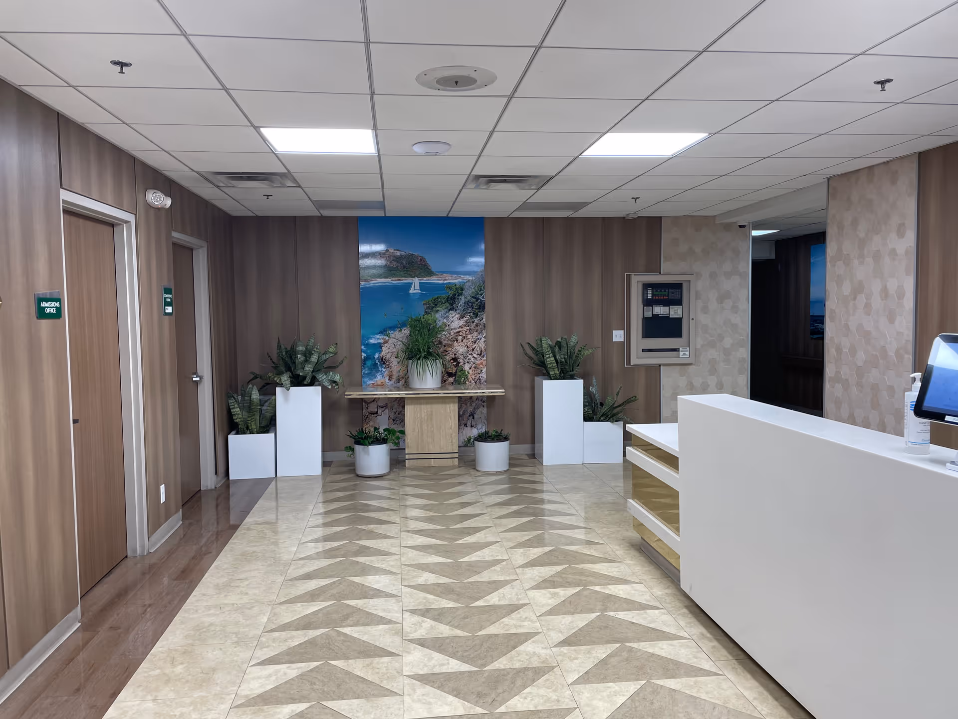 Lobby reception area with a white curved counter, plants, and wall artwork.