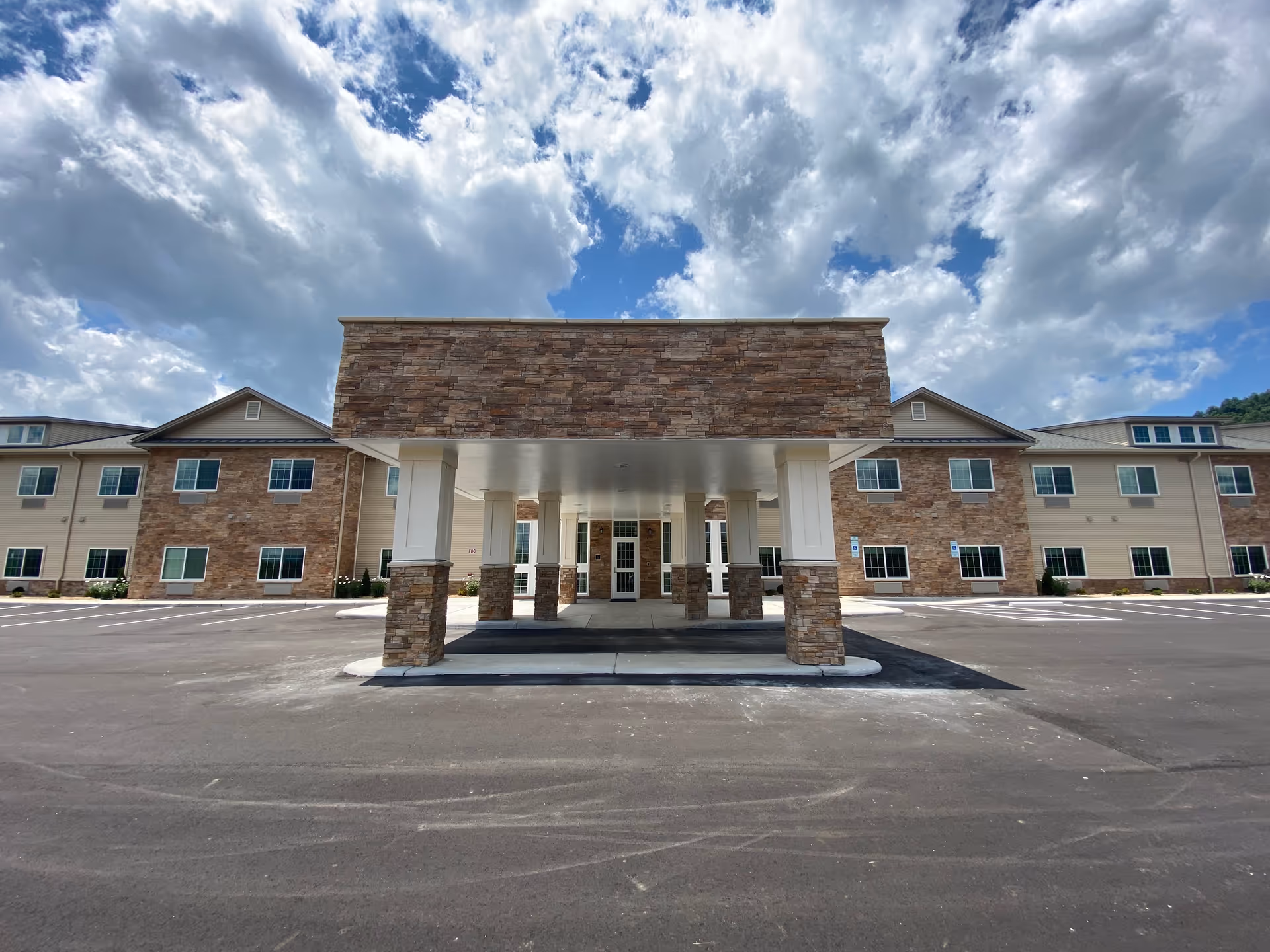 Exterior view of a senior living facility with a stone entrance canopy and parking lot.