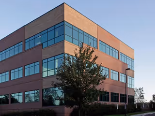 Brick three-story building with expansive blue-tinted windows and a tree.