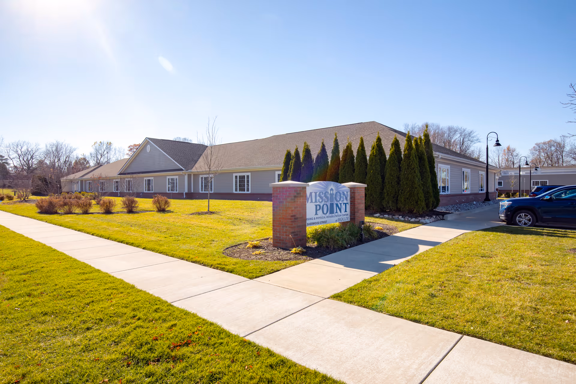 Single-story senior living facility exterior with manicured lawn, trees, and Mission Point sign.