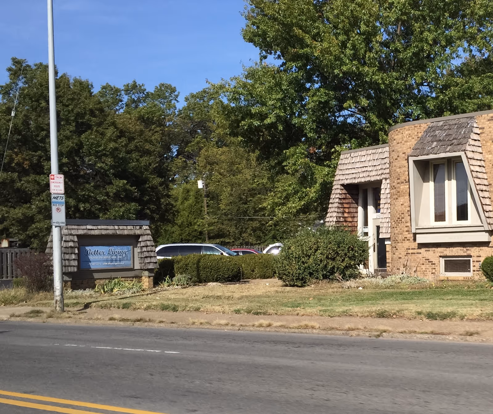 Exterior view of a brick building with a sign reading Better Living near a road.
